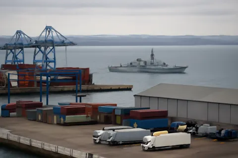 Industrial port worker overlooking bulk-material handling equipment and a cargo vessel.