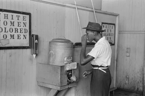 'A person of color drinking at "Colored" water cooler in streetcar terminal, Oklahoma City, Oklahoma' - 35mm nitrate negative of a photo by Russell Lee , depicting the seperate but equal era. Title kept original; obviously language has moved on. Note that, while there is a theoretically higher-resolution source, File:"Colored" drinking fountain from mid-20th century with african-american drinking.jpg , that has some severe damage, like the blur on the left side (below the hand on the sign).