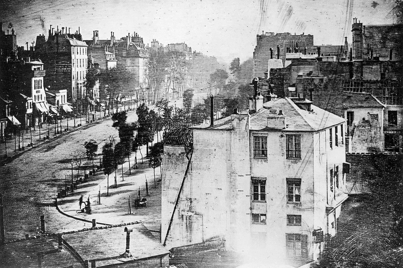Boulevard du Temple , Paris , 3rd arrondissement, Daguerreotype . Made in 1838 by inventor Louis Daguerre , this is believed to be the earliest photograph showing a living person. It is a view of a busy street, but because the exposure lasted for 4 to 5 minutes (see shutter speed Daguerre photo explained ) the moving traffic left no trace. Only the two men near the bottom left corner, one apparently having his boots polished by the other, stayed in one place long enough to be visible. As with most daguerreotypes, the image is a mirror image .