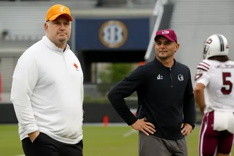 Grounded editorial scene illustrating As the 2026 college football season approaches, all 16 SEC coaches are evaluated for job security, with Shane Beamer of South Carolina notably on the hottest seat.