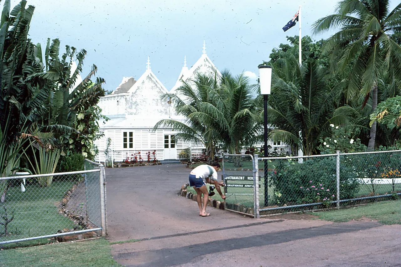 The official residence of the Administrator of the Northern Territory. Also known as the House of the Seven Gables this official building has grown through many extensions since the 1860s. This photo was taken on a camera club outing in1978. Darwin Camera Club member Roy Shepherd is seen opening the gates.