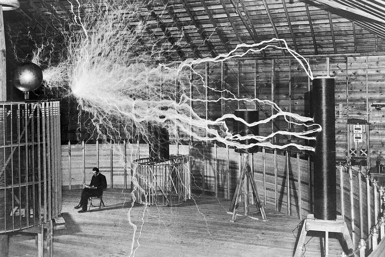 Famous photograph of Serbian-American inventor Nikola Tesla in his laboratory in Colorado Springs December 1899, supposedly sitting reading next to his giant " magnifying transmitter " high voltage generator while the machine produced huge bolts of electricity. The photo was a promotional stunt by photographer Dickenson V. Alley; a double exposure. First the machine's huge sparks were photographed in the darkened room, then the photographic plate was exposed again with the machine off and Tesla sitting in the chair. In his Colorado Springs Notes Tesla admitted that the photo is false: " Of course, the discharge was not playing when the experimenter was photographed, as might be imagined! " Tesla's biographers Carl Willis and Mark Seifer confirm this. During 1899-1900 Tesla built this laboratory and researched wireless transmission of electric power there. The Magnifying Transmitter, one of the largest Tesla coils ever built, with input power of 300 kW could produce potentials of around 12 million volts at a frequency of about 150 kHz, creating 130 ft. (41 m) "lightning bolts". The arcs in the image are 22 feet long. These long arcs were not a feature of the normal operation of the coil because they wasted energy; for these photos Tesla forced the machine to produce arcs by switching the power rapidly on and off. The photo was part of a publicity spread taken by photographer Dickinson Alley in December 1899 to accompany Tesla's magazine article Nikola Tesla, "The Problem of Increasing Human Energy", Century Magazine , The Century Co., New York, June 1900, fig. 8 ; a version without Tesla appears in the article. Wellcome Images Keywords: Electrical energy; Electric; Power; Electricity; Energy; Volt; Power (Psychology); Static; Voltage; Laboratories; Nikola Tesla