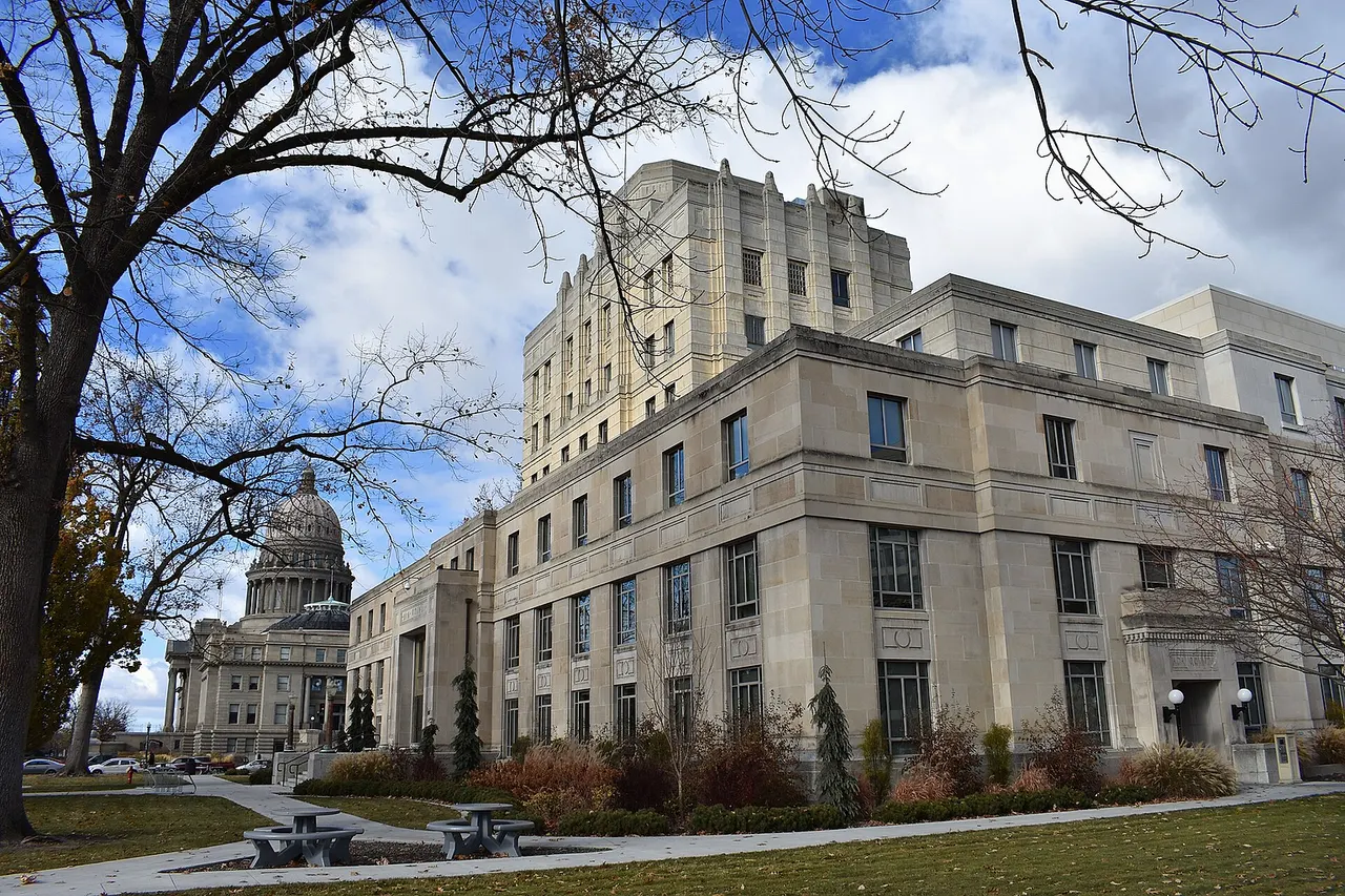 At right are the West Jefferson Street and North 5th Street exposures of the Old Ada County Courthouse (1939), designed by Tourtellotte & Hummel and Wayland & Fennell, and in the distance is the Idaho State Capitol Building (1912 and 1920), designed by Tourtellotte & Hummel. The buildings are part of the Boise Capitol Area District and listed on the National Register of Historic Places.