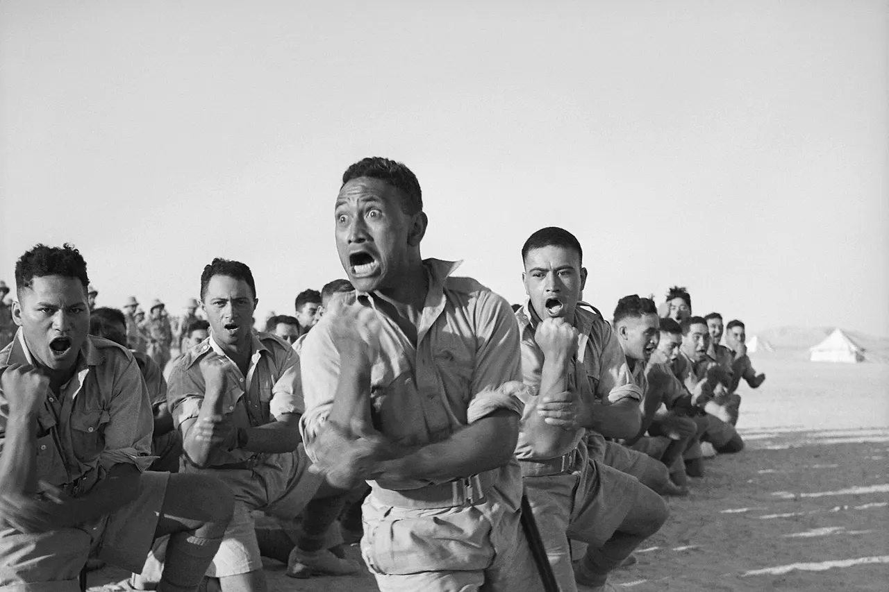 Māori Battalion survivors of action in Greece, performing a haka in Helwan , Egypt for the King of Greece . From left to right, the four men in the foreground are John Manuel, Maaka White, Te Kooti Reihana, and Rangi Henderson. A cropped version of this photo featured on an ANZAC commemorative stamp issued in 2008. [2]