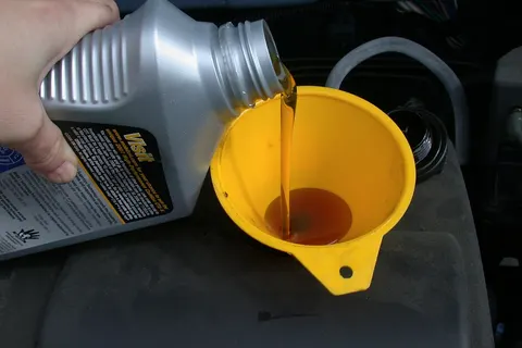 Using a funnel to refill the motor oil in an automobile as part of an oil change.