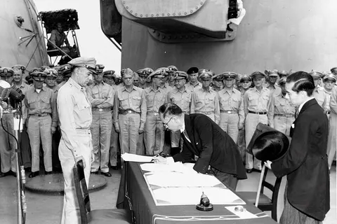 Japanese Foreign Minister Mamoru Shigemitsu signs the Instrument of Surrender on behalf of the Japanese Government, on board USS Missouri (BB-63) , 2 September 1945. Lieutenant General Richard K. Sutherland, U.S. Army, watches from the opposite side of the table. Foreign Ministry representative Toshikazu Kase is assisting Mr. Shigemitsu.
