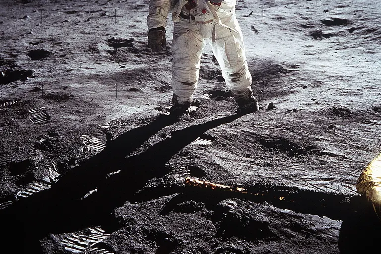 Short description : Astronaut Buzz Aldrin on the Moon Full description : Astronaut Buzz Aldrin , Lunar Module pilot, walks on the surface of the Moon near the leg of the Lunar Module (LM) "Eagle" during the Apollo 11 extravehicular activity (EVA). Astronaut Neil A. Armstrong , commander, took this photograph with a 70mm lunar surface camera. While astronauts Armstrong and Aldrin descended in the Lunar Module (LM) "Eagle" to explore the Sea of Tranquility region of the Moon, astronaut Michael Collins, command module pilot, remained with the Command and Service Modules (CSM) "Columbia" in lunar orbit. Variations : The upper black band is an addition to the original photo, carried out for "reasons of balance". See the original photo and the explanation of the edit at NASA's website . In the expanded version of the photo, it is possible to see a horizontal white line at the top left (viewer's right) of the helmet. This is the base of the antenna that was cut in the original frame of the photo.