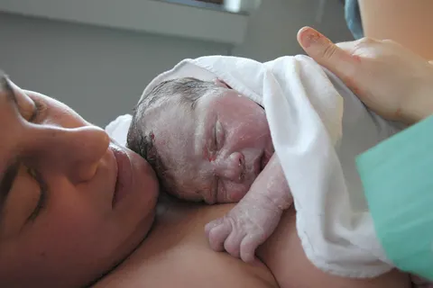 Baby on mother's belly right after birth, skin covered in vernix and some blood.