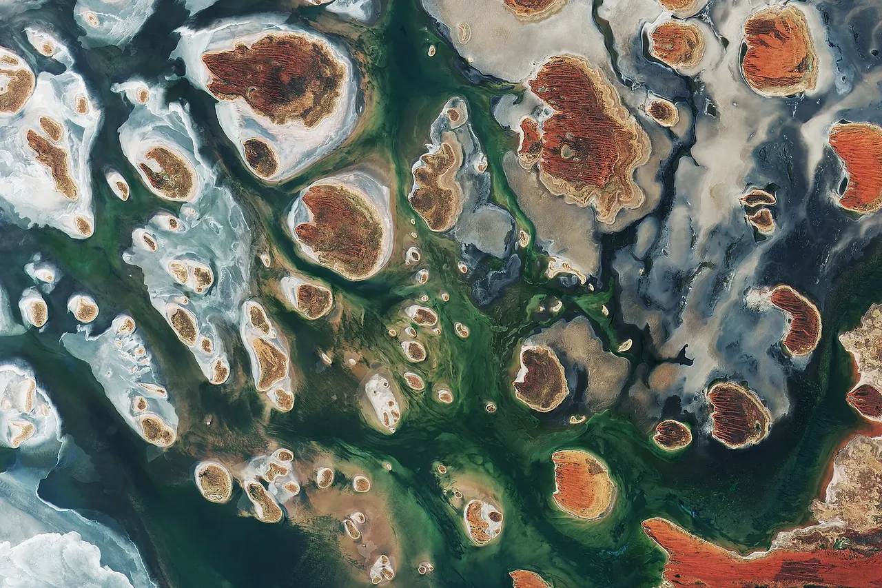 Lake Mackay , Australia, by Copernicus Sentinel-2B satellite. Brown hills speckle the eastern part of Australia’s Lake Mackay in this satellite image. Located on the border of the states of Western Australia and Northern Territory, the salt lake only sees water after seasonal rainfall – if at all. It is classified as an ephemeral lake, meaning it exists only after precipitation. This is not the same as a seasonal lake, which sees water for longer periods. About half of Australia's rivers drain inland and often end in ephemeral salt lakes. The greens and blues in this image show desert vegetation or algae, soil moisture and minerals – mainly salt. On some of the brown ‘islands’ and on the shore in the lower right, we can see the east–west sand ridges forming lines in the landscape. The lake lies at the edge of the Great Sandy Desert , which covers nearly 285,000 sq km. Roads are scarce in the area, and often frequented by four-wheel drive adventurers. Roads include the Canning Stock Route about 300 km to the west of the image, or Tanami Track connecting Australia’s Stuart Highway to the Great Northern Highway around 300 km to the east.