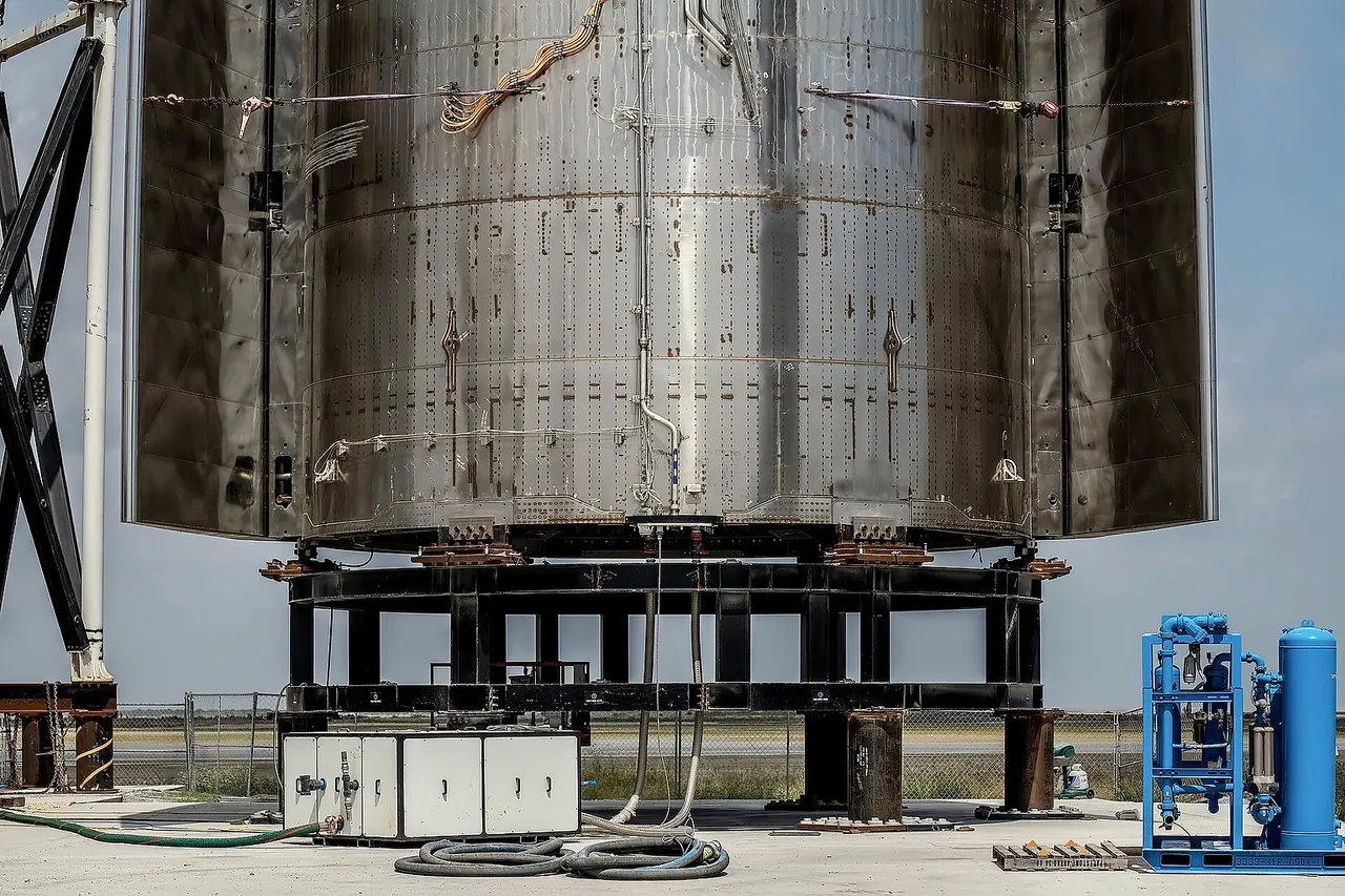 A vertical panorama of Starship SN16 spacecraft taken on 5 September 2021 at SpaceX's Starbase spaceport, which at the time was intended to fly after Starship SN15. However, as of January 2022, the prototype is cancelled and waiting for recycling. Both of its forward and aft flap pairs are closed, with cables and piping seen running in the middle of the spacecraft. Welding seams of steel sections can be seen very clearly, and machines surrounding the spacecraft demonstrate the size of its height.
