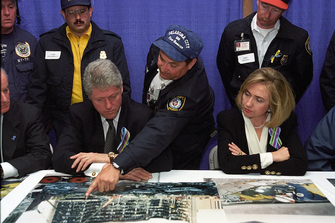 President Bill Clinton and First Lady Hillary Rodham Clinton meet with the heads of the search and rescue teams for a briefing held at the Oklahoma State Fairgrounds arena on the day of the memorial service for the victims of the truck bombing of the Alfred P. Murrah Federal Building. A representative from the Oklahoma City Fire and Rescue department stands between the President and First Lady and points to an area on an enlarged photo of the building remains at the bombing site. Photographer: Ralph Alswang
